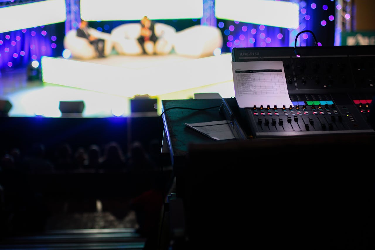 contact-img Sound console in a studio setting for a live event with blurred audience view.