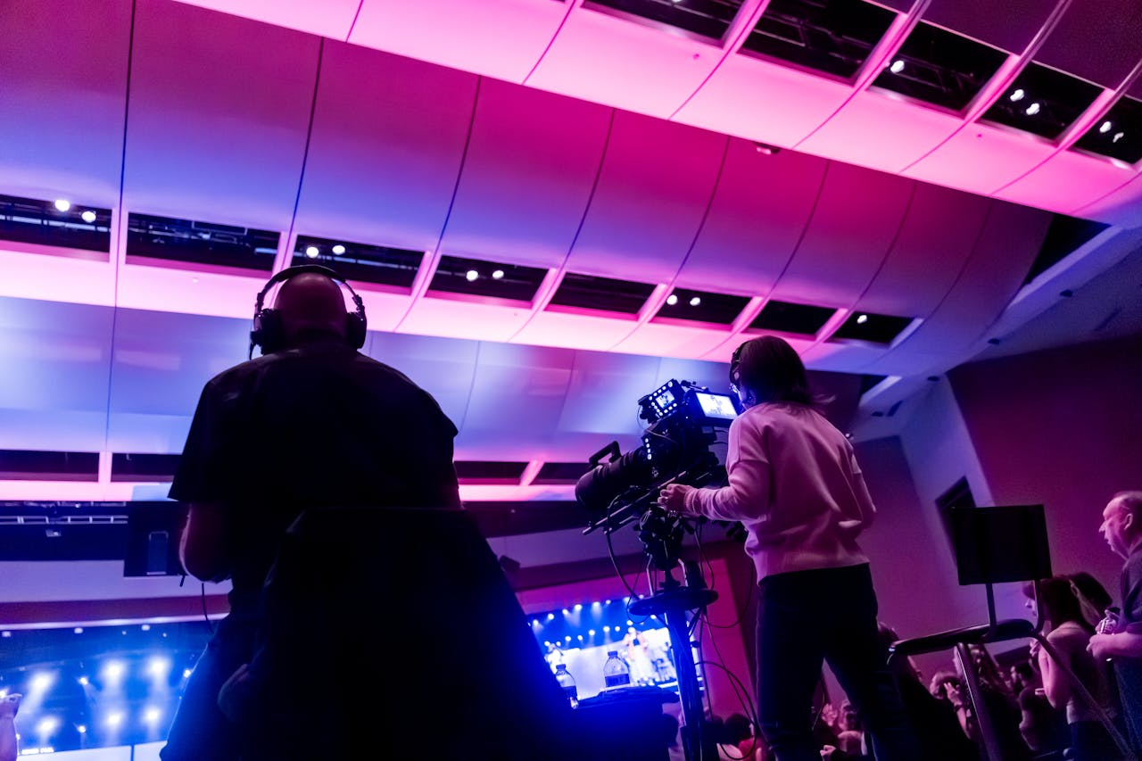 about-img-01 Professional camera crew filming a live event indoors, capturing vibrant stage lighting.