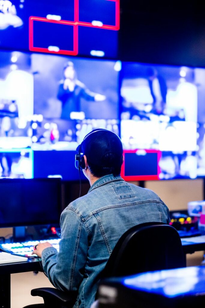 pexels photo 11258760 11258760 Man in a denim jacket working in a modern studio with multiple screens displaying images.